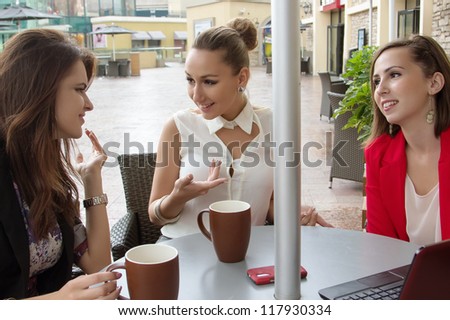 Group of three young women communicating in cafe. Friends are sitting at table outdoor and talking