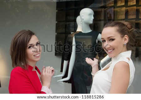 Young women shopping at the mall for a new dress, looking at a store window and want to buy it
