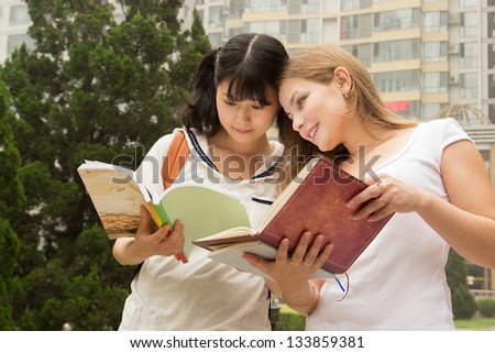 Young women reading book in the green park. Students are studying, learning outdoor