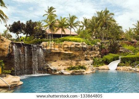Beautiful tranquil deserted tropical resort rock pool with a waterfall feature and water slide surrounded by palm trees for an idyllic summer vacation