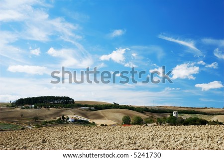 Pale blue and white sky over cultivated land and old church