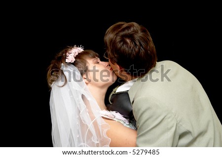 The young bride kisses the groom on a black background