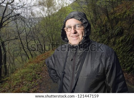 Mature man with a raincoat in nature. The man wearing glasses and looking at camera. The portrait is made with Flash Light