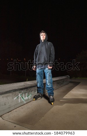 Rollerskater in a skateboard park at night. The man is stand and looking at camera.
