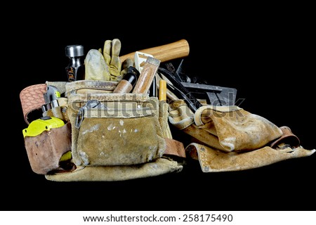 Rugged worn carpenters leather work bags and belt with construction tools and hammer isolated on black and selective focus on plumb.