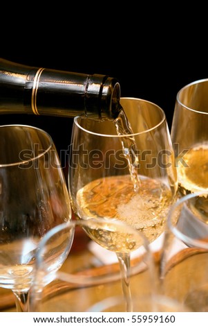 White wine pouring on glasses on a party. Black background