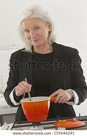good looking senior cooking in her kitchen with orange pan