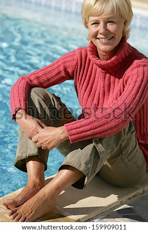 Senior Lady Sitting by the Pool in sunny day of spring time still wearing winter clothes
