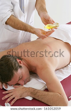 Man  on a massage table is having his low back massaged by a masseur putting oil