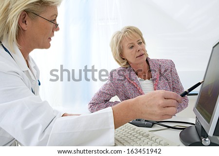 female doctor sitting at her desk pointing to a computer screen explaining something to a senior woman patient