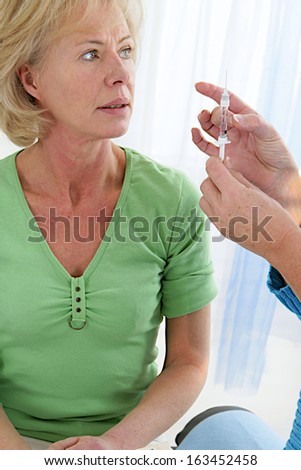 Doctor preparing an against flu vaccine to a middle aged woman patient