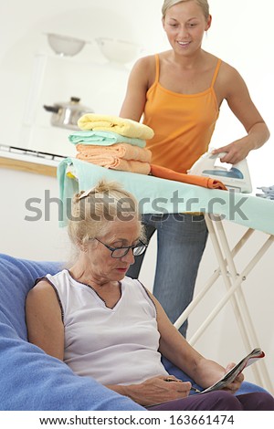 Closeup of elderly woman reading a magazine with home help ironing