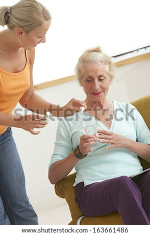 Home-care young girl helping elderly lady to take her medicine.