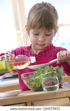 Child girl preparing sauce for green salad focus on oil flowing in the spoon