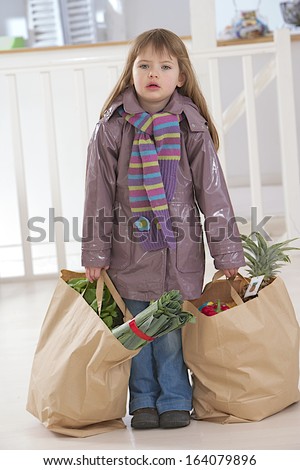 cute little girl holding 2 bags full of food products, fruits and vegetables like a woman