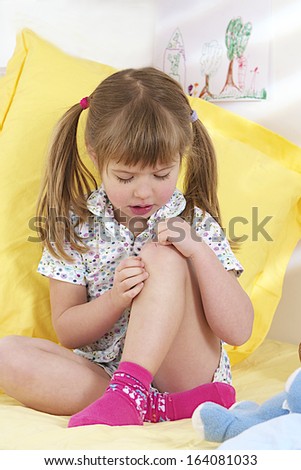 cute little girl on the sofa looking at her bleeding knee