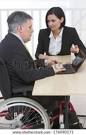 Businessman in wheelchair with assistant in office