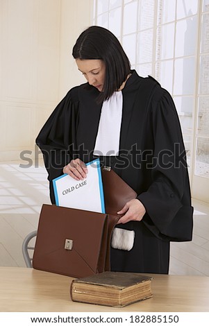 Law court or justice concept. Young woman lawyer attorney wearing classic  french black white gown stowing a cold case  file folder in her briefcase