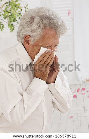 Elderly man blowing his nose and suffering from pollen allergy  profile view