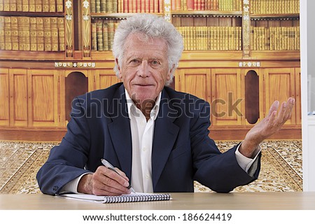 Senior business man writing at his desk and  raising  hand