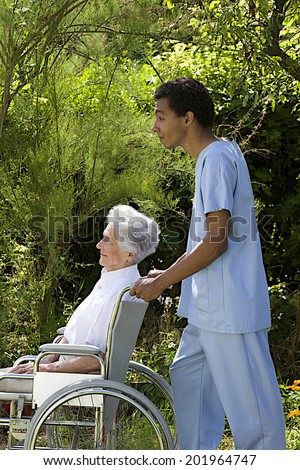 Young hospital staff pushing  happy senior patient in wheelchair outdoors