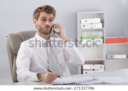 Portrait of a young man sitting at a desk phoning and writing on a document