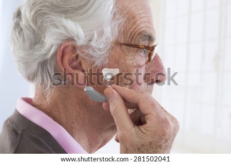 Closeup of a senior man inserting a hearing aid in her hear