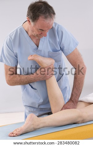 Physiotherapist stretching his patients leg in medical office