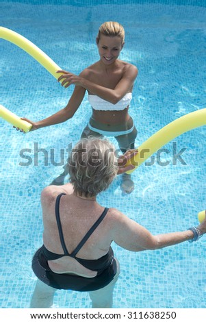 Therapist and  senior woman  doing aqua fitness  with swim noodles