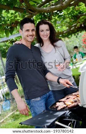 happy young loving couple cooking  together at barbecue party with a glass of wine in summertime
