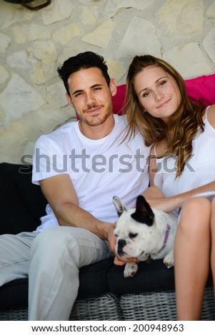 happy and cheerful young couple man woman with pet dog french bulldog sitting outdoor in sofa