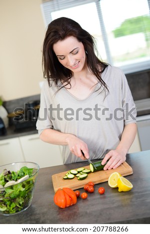 cheerful young woman preparing an organic fresh vegetables salad for lunch in kitchen for summer party