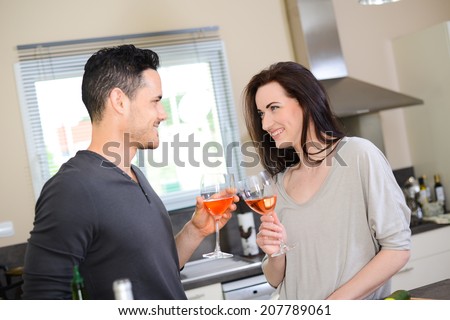 happy beautiful young couple together in kitchen cheering with a glass of wine while preparing salad with organic vegetables for lunch summer party