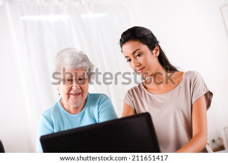 cheerful young woman teaching computer and internet to an elderly person