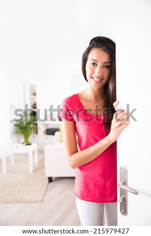 cheerful young woman opening her house front door and inviting friends at home