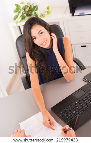 cheerful young brunette business woman holding a pen to customer and inviting to sign a contract
