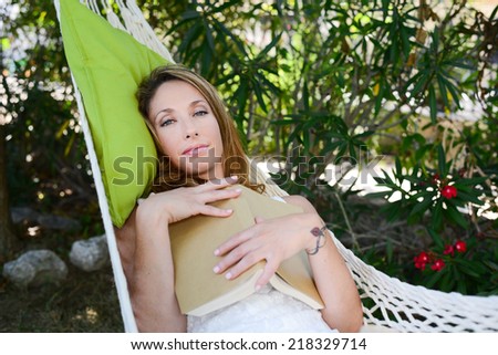cheerful young woman relaxed reading a book in a hammock in a peaceful garden during summer holiday