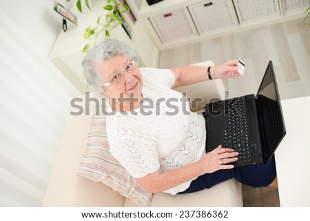 cheerful elderly woman web surfing and shopping on internet at home with laptop