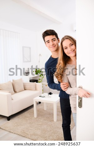 happy young couple opening door and welcoming their friends in apartment