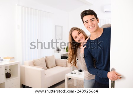 happy young couple opening door and welcoming their friends in apartment