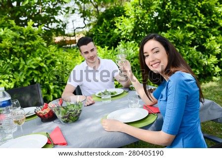 cheerful young couple man and woman cheering with a glass of wine outdoor in a summer barbecue garden party