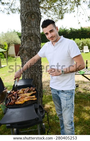 handsome young man cooking meat on barbecue outdoor during summer