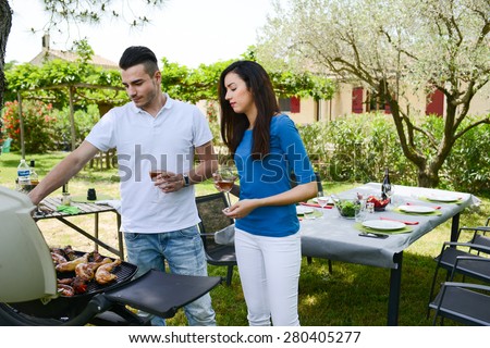 cheerful young couple man and woman cooking barbecue outdoor in a summer garden party