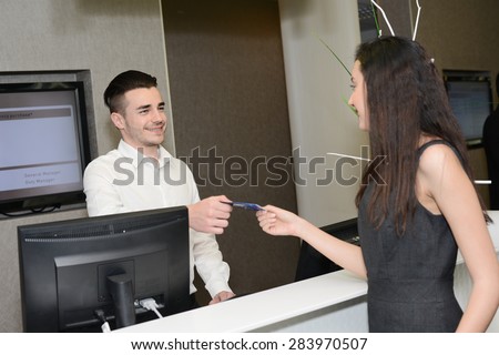 handsome young man receptionist handing over room keys to a beautiful woman in hotel front desk