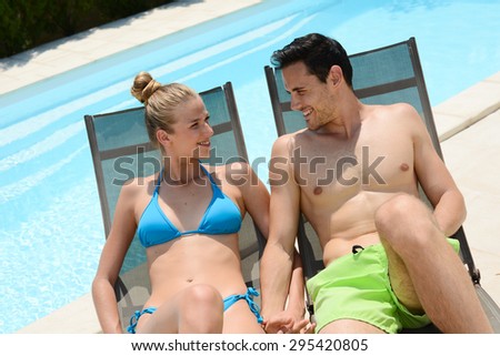 beautiful young couple in swimsuit relaxed in deck chairs by the pool