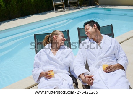 beautiful young couple resting in deck chairs with bathrobe by the pool of a thalasso resort