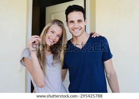 happy young couple man and woman handing over their new home keys in front of open house door
