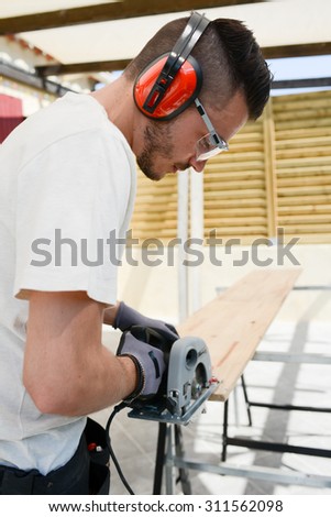handsome young man carpenter working with electric tool on wood timber in construction site