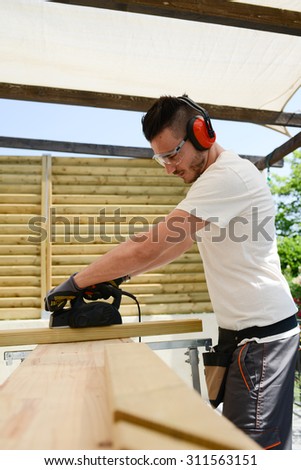 handsome young man carpenter working with electric tool on wood timber in construction site