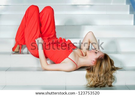 Cute young woman in a red pantsuit lying on the stairs